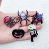 Un juego de diez colgantes de acrílico para Halloween con diseños de araña, murciélago y calabaza en una mano.