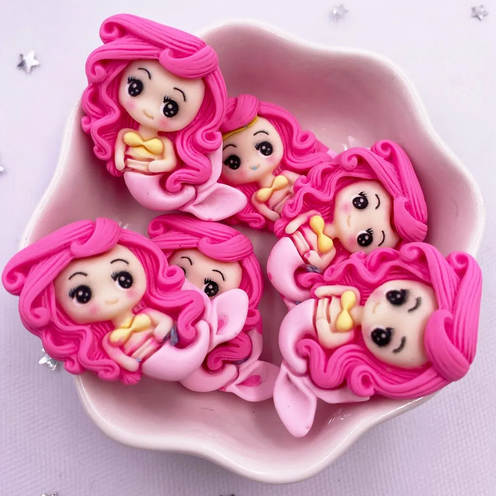 Pink resin figurines of mermaid princesses with curly hair displayed in a pink dish.