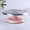 A pink ceramic cake turntable with a silver aluminum top resting on a white surface.