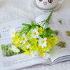 A bouquet of artificial white and yellow daisy flowers with green foliage displayed on an open book.