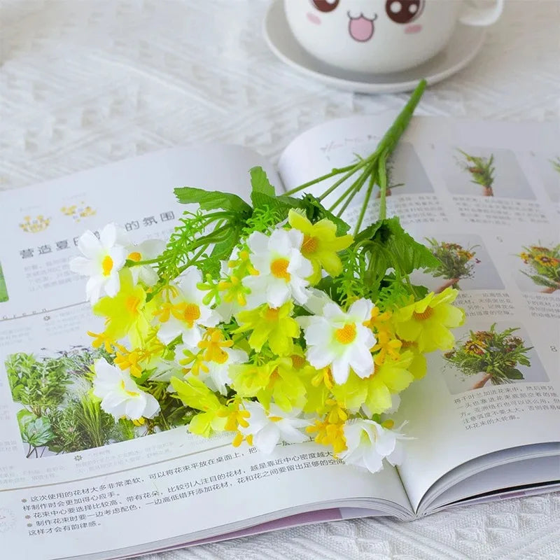 A bouquet of artificial white and yellow daisy flowers with green foliage displayed on an open book.