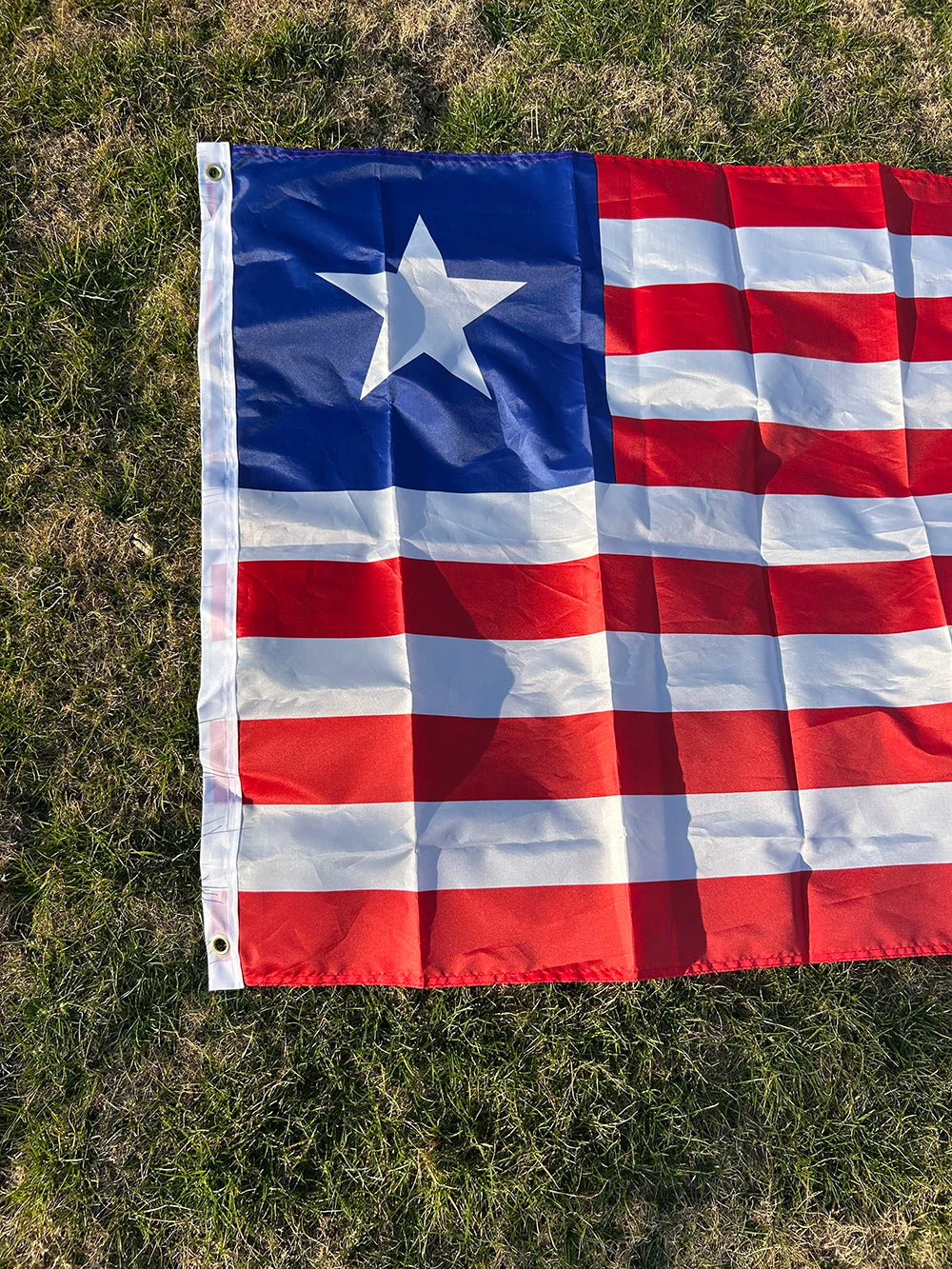 A decorative banner displaying the flag of Liberia, featuring blue, white, and red stripes and a white star on a green lawn.
