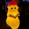 A cute ghost night light shaped like a figure reading a book, glowing yellow with a red hat.