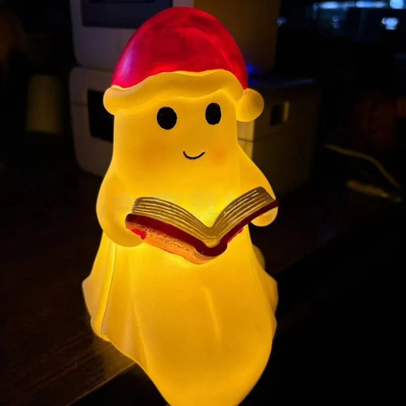 A cute ghost night light shaped like a figure reading a book, glowing yellow with a red hat.