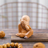 A small, tan resin figurine of a monk with a shaved head and folded hands sitting on a wooden surface.