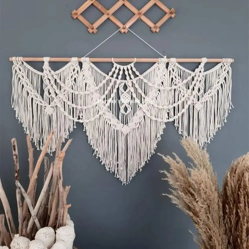 Handwoven boho macrame wall hanging tapestry with fringe in off-white color against a gray wall.