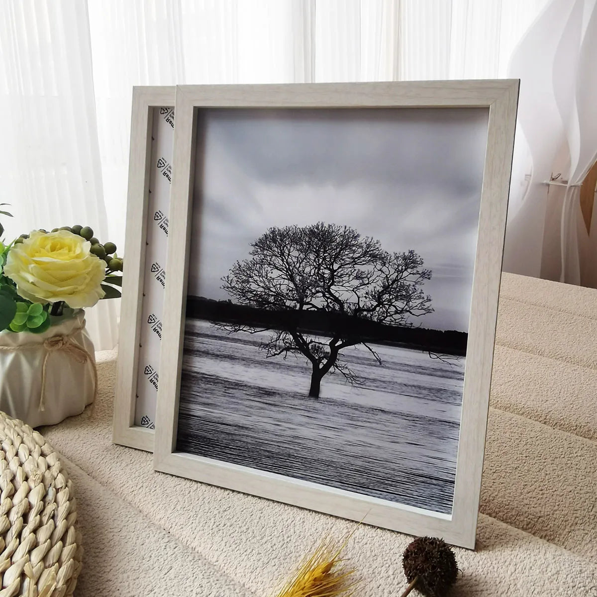 A wooden photo frame displaying a black silhouette of a tree against a cloudy sky and a flat landscape.
