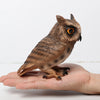 A realistic figurine of an owl perched on a human hand.