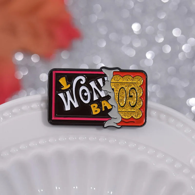 A black enamel lapel pin featuring gold lettering that reads WON BA with a stylized silhouette of a tree.