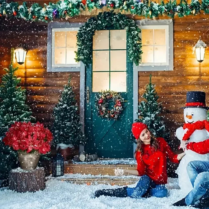 A woman in a red sweater sits in the snow in front of a decorated house with Christmas trees and a wreath.