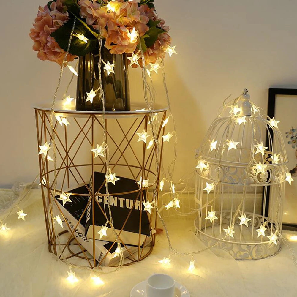 A display featuring LED star fairy lights draped around a gold wire cage and a glass birdcage.