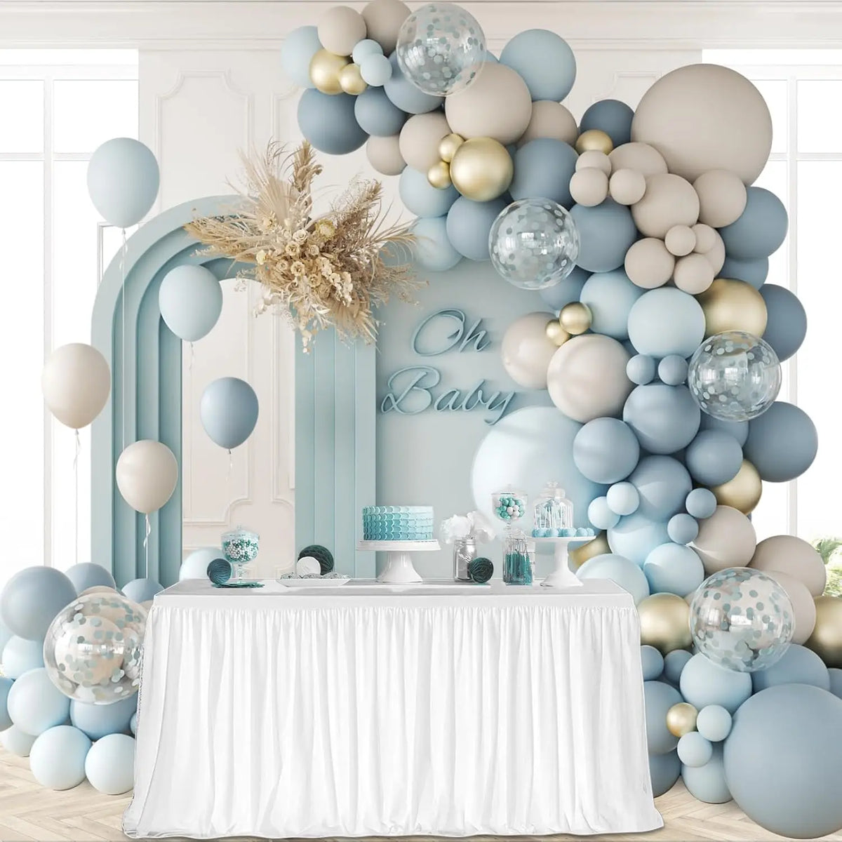 Decoración para baby shower con arco de globos azul y beige sobre una mesa cubierta con tela blanca.