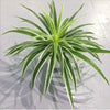 A vibrant green artificial chlorophytum branch with long, pointed leaves displayed on a light surface.