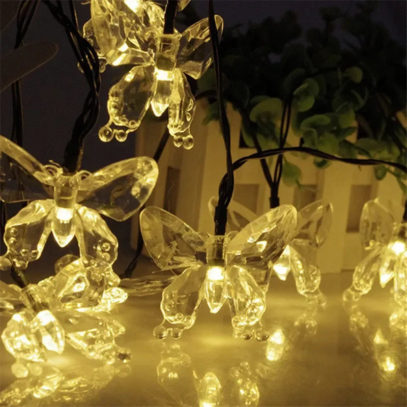 A close-up of solar decorative string lights shaped like butterflies illuminating a dark outdoor setting.
