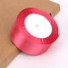 A roll of bright pink satin ribbon for crafts and gift wrapping, resting on brown kraft paper.