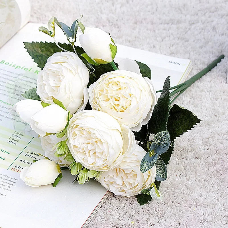 A bouquet of white silk roses and peonies with green leaves displayed on a white background.