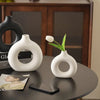 White ceramic vase with a donut pattern holding a single white tulip on a dark table.