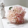 A large bouquet of pink and white silk hydrangea flowers next to a white angel figurine.