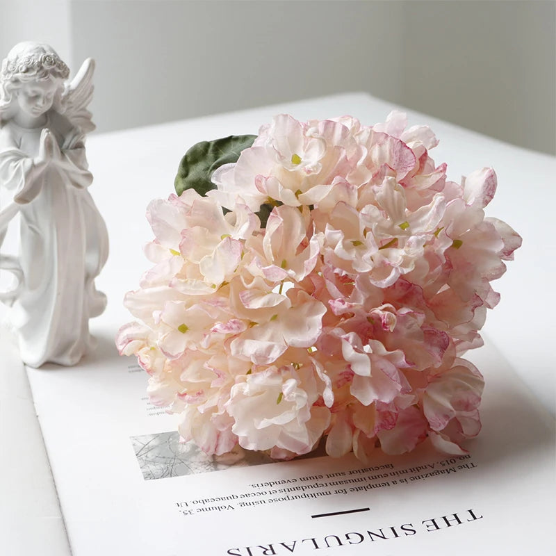 A large bouquet of pink and white silk hydrangea flowers next to a white angel figurine.