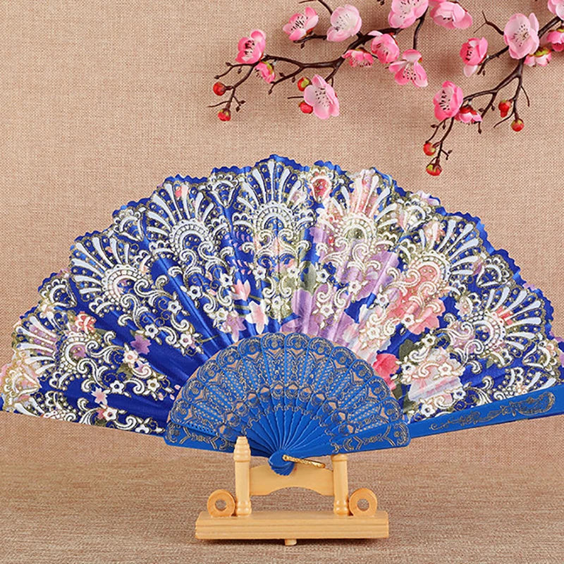 A blue and pink silk flower folding fan displayed on a wooden stand against a beige background.