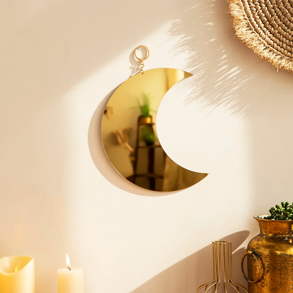 A gold moon acrylic wall mirror with a loop hanger mounted on a beige wall.