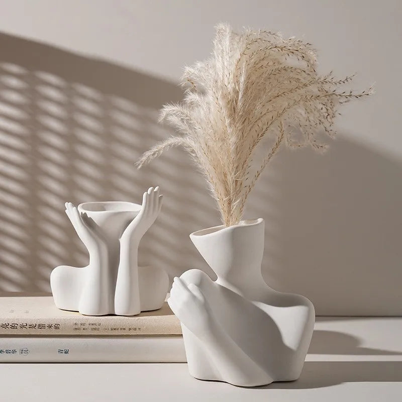 A white ceramic figural vase shaped like an artistic human form holds dried ornamental grass.
