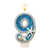 A decorative number 9 candle made of glitter and blue sequins with a flame on top.