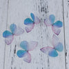 A collection of delicate, translucent blue and pink organza butterfly embellishments for jewelry making displayed on a white 