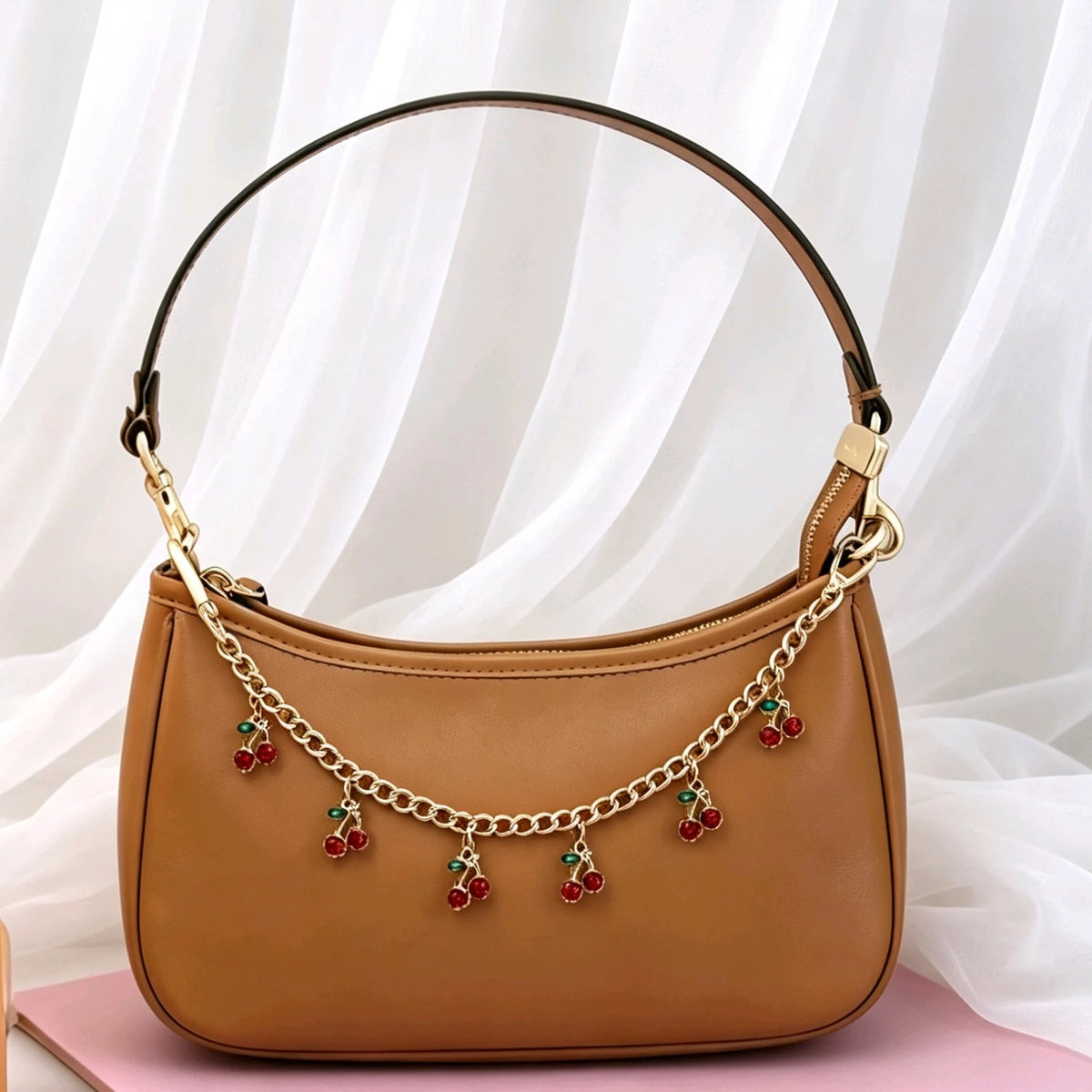 A tan leather pouch with a gold chain and multiple red cherry charm decorations.