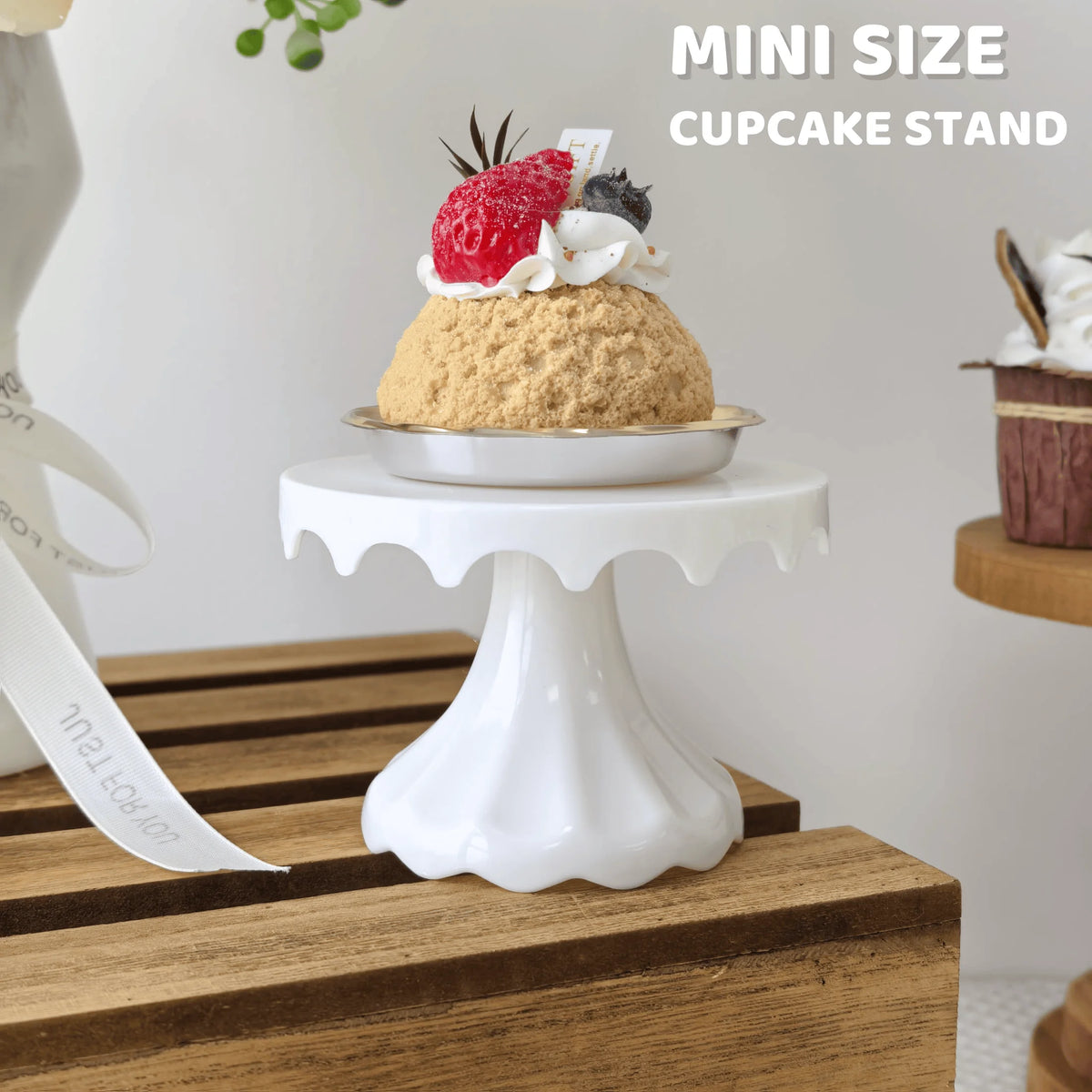 A mini cupcake stand displaying a single cupcake with cream and strawberry on a white pedestal.