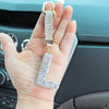 A hand holds a crystal letter keychain charm with a gold bail and silver chain.