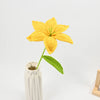 Hand-crocheted yellow lily flowers with green stems displayed in a white vase.