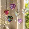 A collection of iridescent crystal heart pendants hanging in front of a bright window.