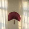 A pink handwoven bamboo wall fan decor with a tassel mounted on a white wall.