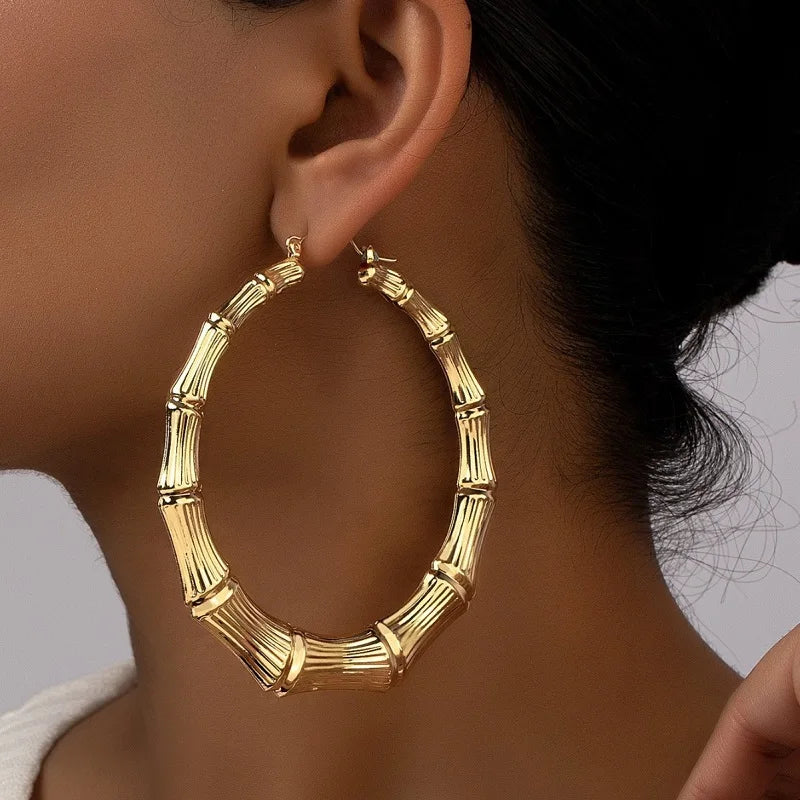 A close-up of oversized gold bamboo hoop earrings worn on a person's ear.