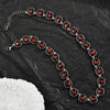 A necklace featuring red crystal pendants strung together on a silver chain, displayed on black fabric.