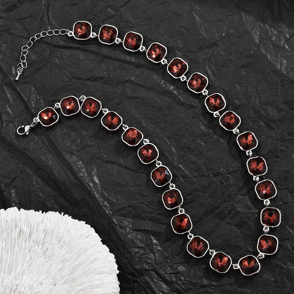 A necklace featuring red crystal pendants strung together on a silver chain, displayed on black fabric.