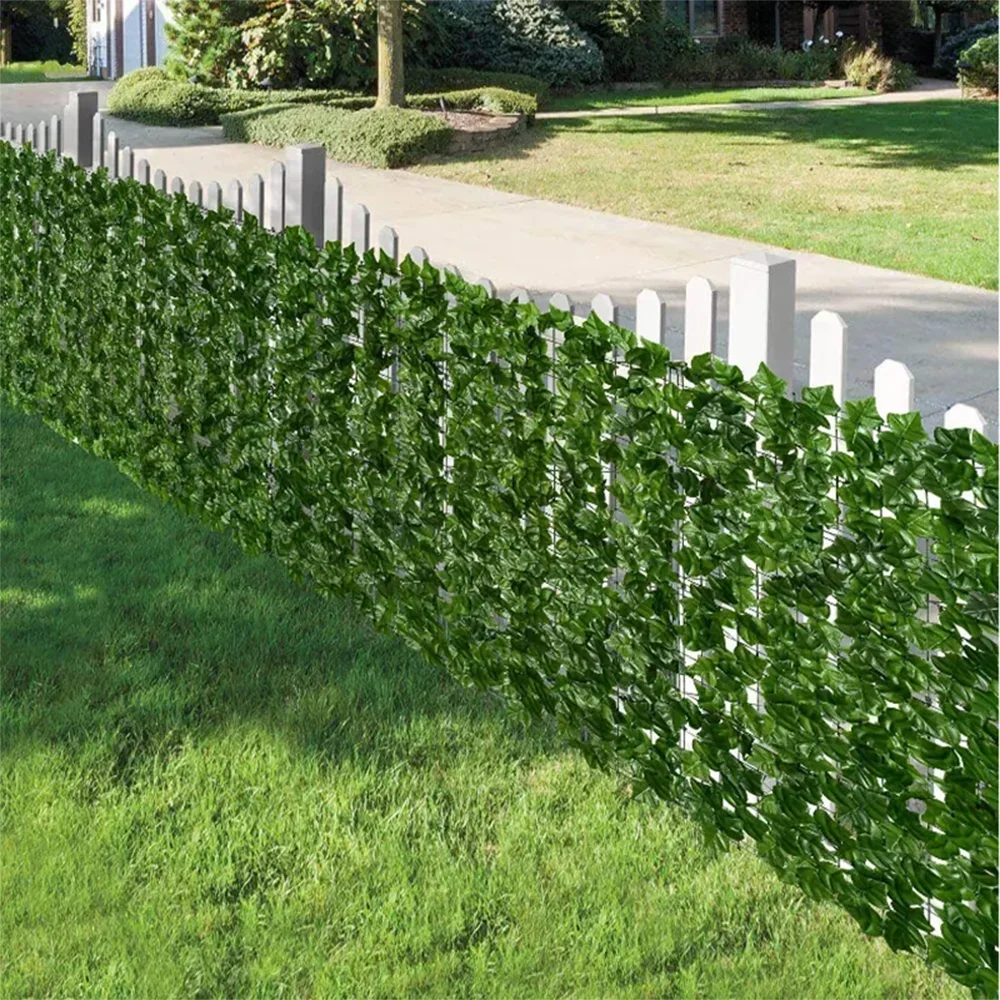 A long row of artificial ivy hedge fence panels lining a walkway and lawn.