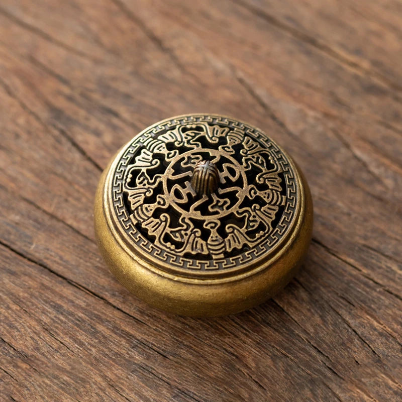 A round, brass incense burner holder with intricate geometric patterns resting on a dark wooden surface.