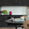 A dark wood table with a white cup and some books set against a background of black floral wallpaper.