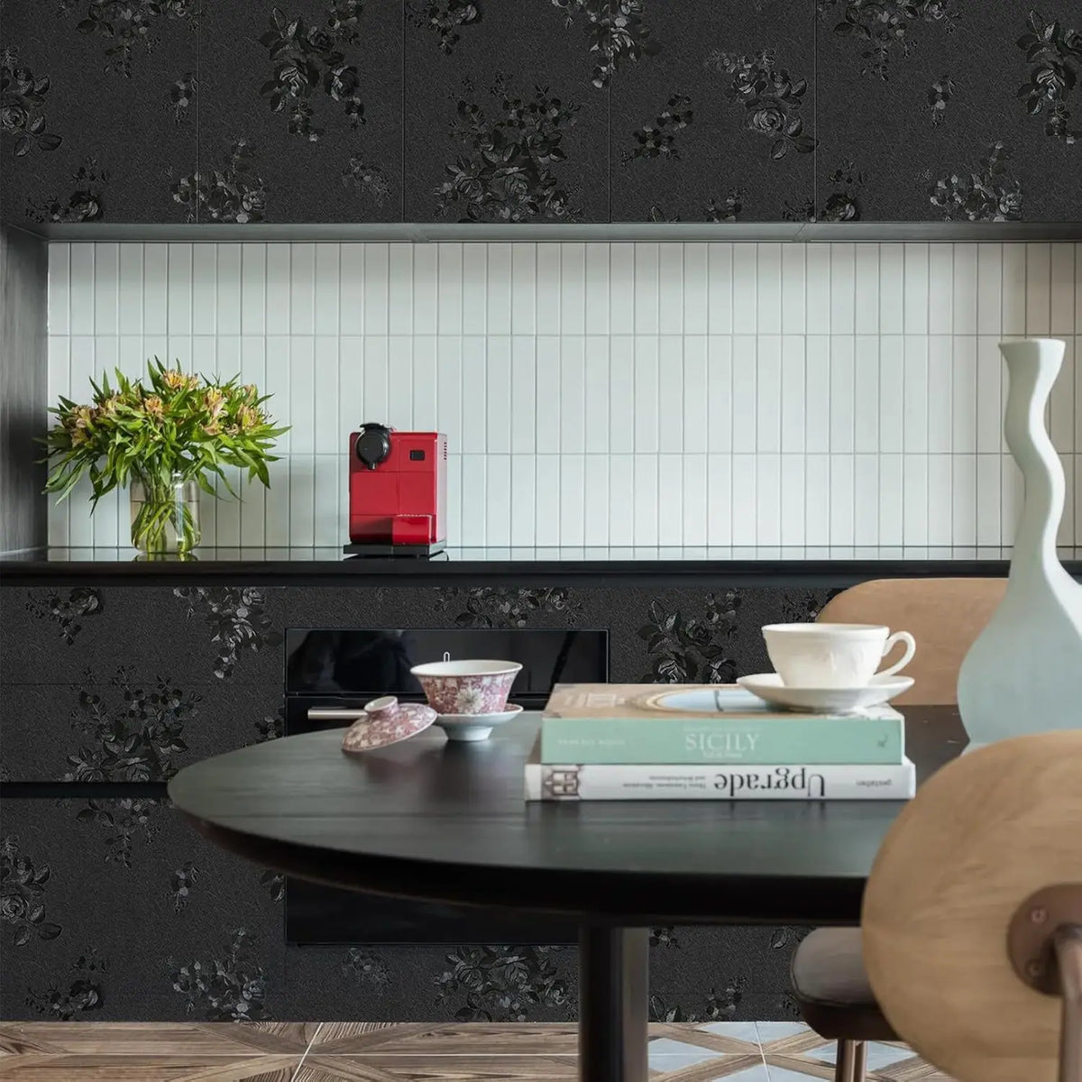 A dark wood table with a white cup and some books set against a background of black floral wallpaper.