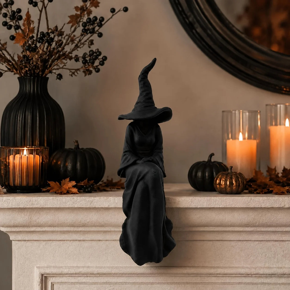 A black witch figurine with a pointed hat and flowing cloak decorates a mantelpiece with pumpkins and candles.
