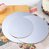 A silver coated round cake board is shown on a wooden cutting board next to a cake and printed paper.