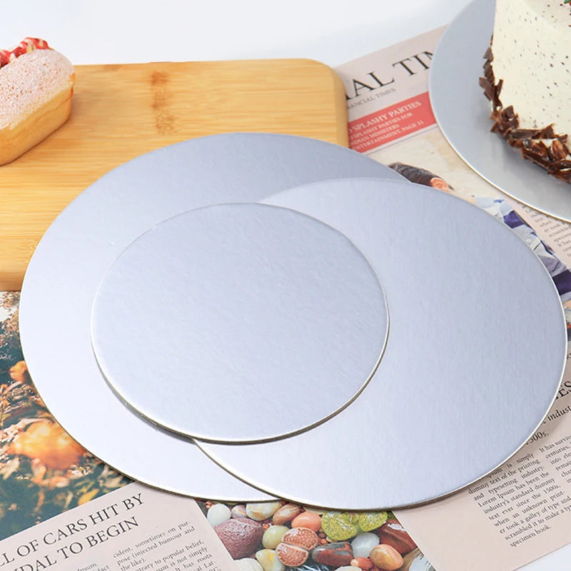 A silver coated round cake board is shown on a wooden cutting board next to a cake and printed paper.