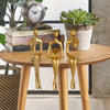 Three gold abstract thinker sculptures displayed on a wooden table next to books and a potted succulent.