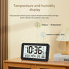A digital wall clock display showing the time 10:36, temperature, and indoor humidity percentage on a wooden surface.