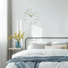 A modern wall clock with gold 3D numerals hangs on a white wall above a bed.