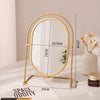 A gold-framed oval vanity mirror with a rotating stand is displayed on a white surface.