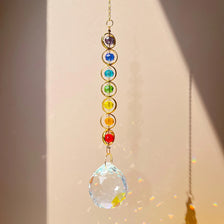 A delicate gold chain holds a string of colorful crystal beads, culminating in a clear glass sphere.
