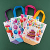 A set of colorful reusable happy birthday gift bags with pink, blue, and purple handles are displayed on a green background.